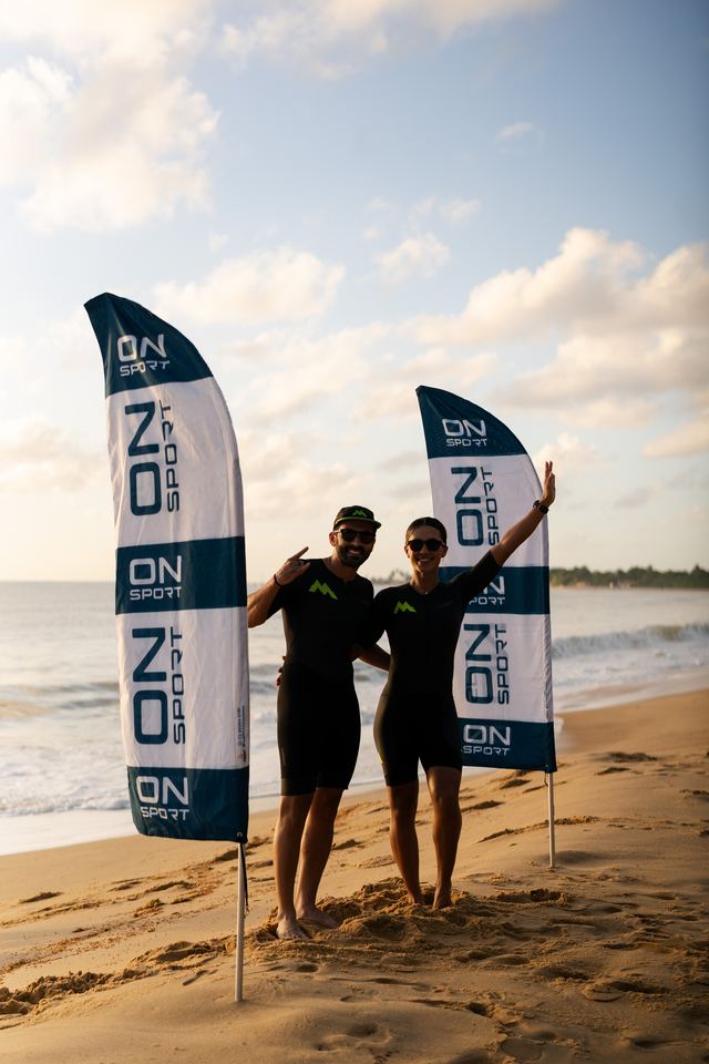 Dupla posando com as bandeiras ON SPORT na praia