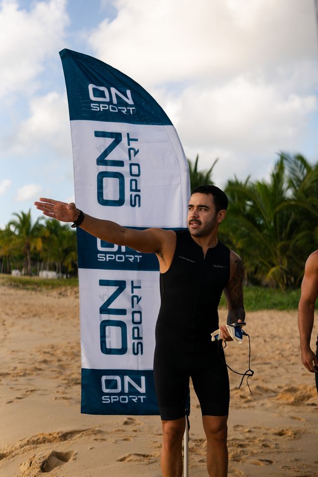 Atleta apontando o percurso ao lado da bandeira ON SPORT