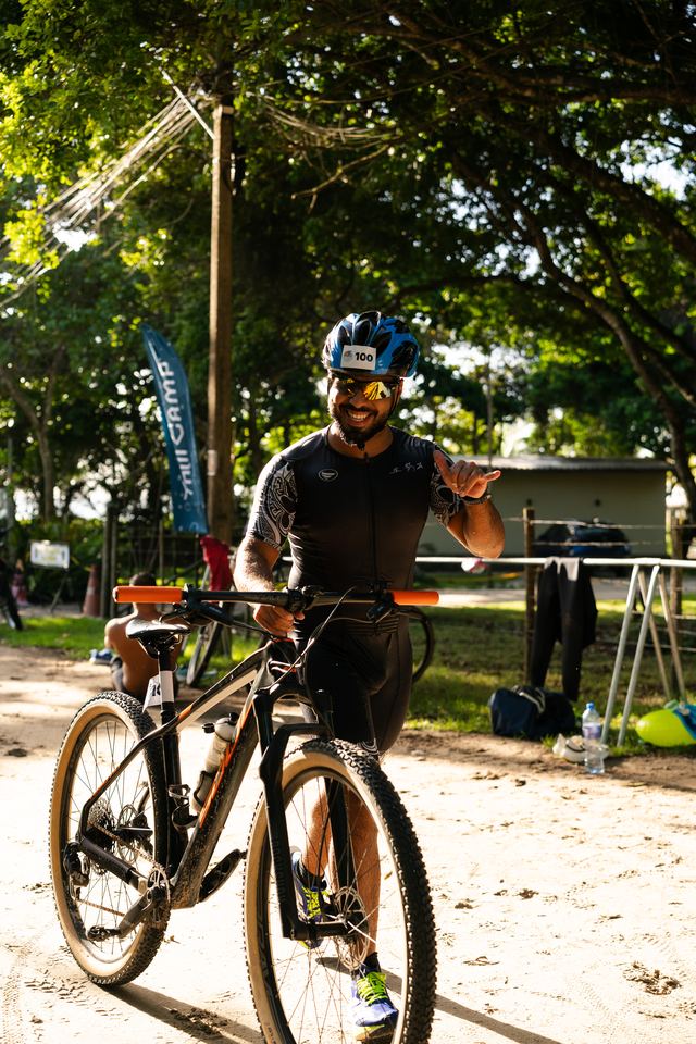 Atleta sorrindo e fazendo o sinal de hang loose com a bike