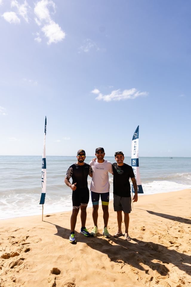 Trio de atletas na praia, ao lado da bandeira ON SPORT